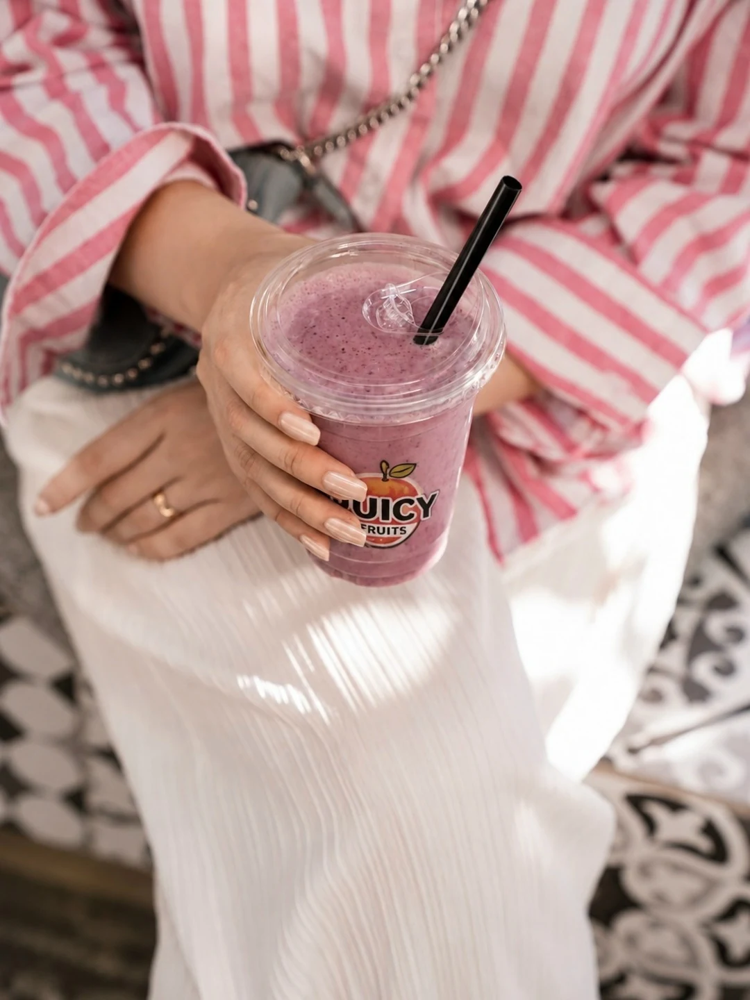 Стакан JUICY FRUITS с розово-ягодным напитком и прозрачной крышкой в руках на фоне полосатой рубашки